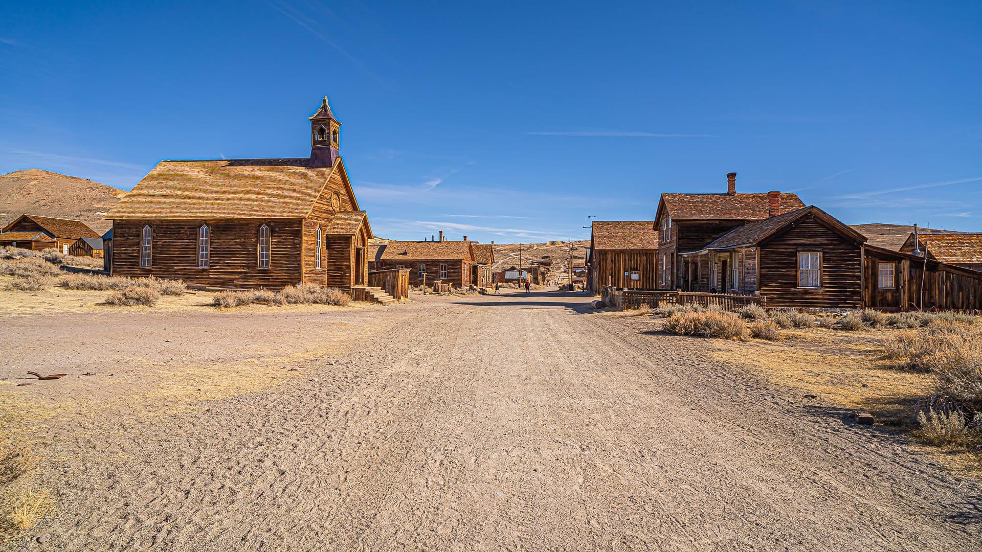 An empty dirt street running through a weathered ghost town